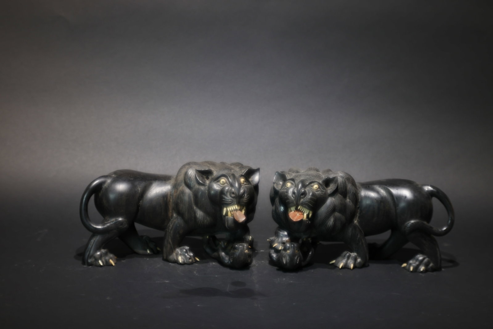 A Pair of Ebony and Ivory-Inlaid 'Foo Dogs' Carvings, Late Qing Dynasty: Estimated Date: Late Qing Dynasty. A pair of ebony carved guardian lion scholar’s desk ornaments.Attribution: Expertly carved from solid ebony, this matched pair depicts powerful striding guardian l