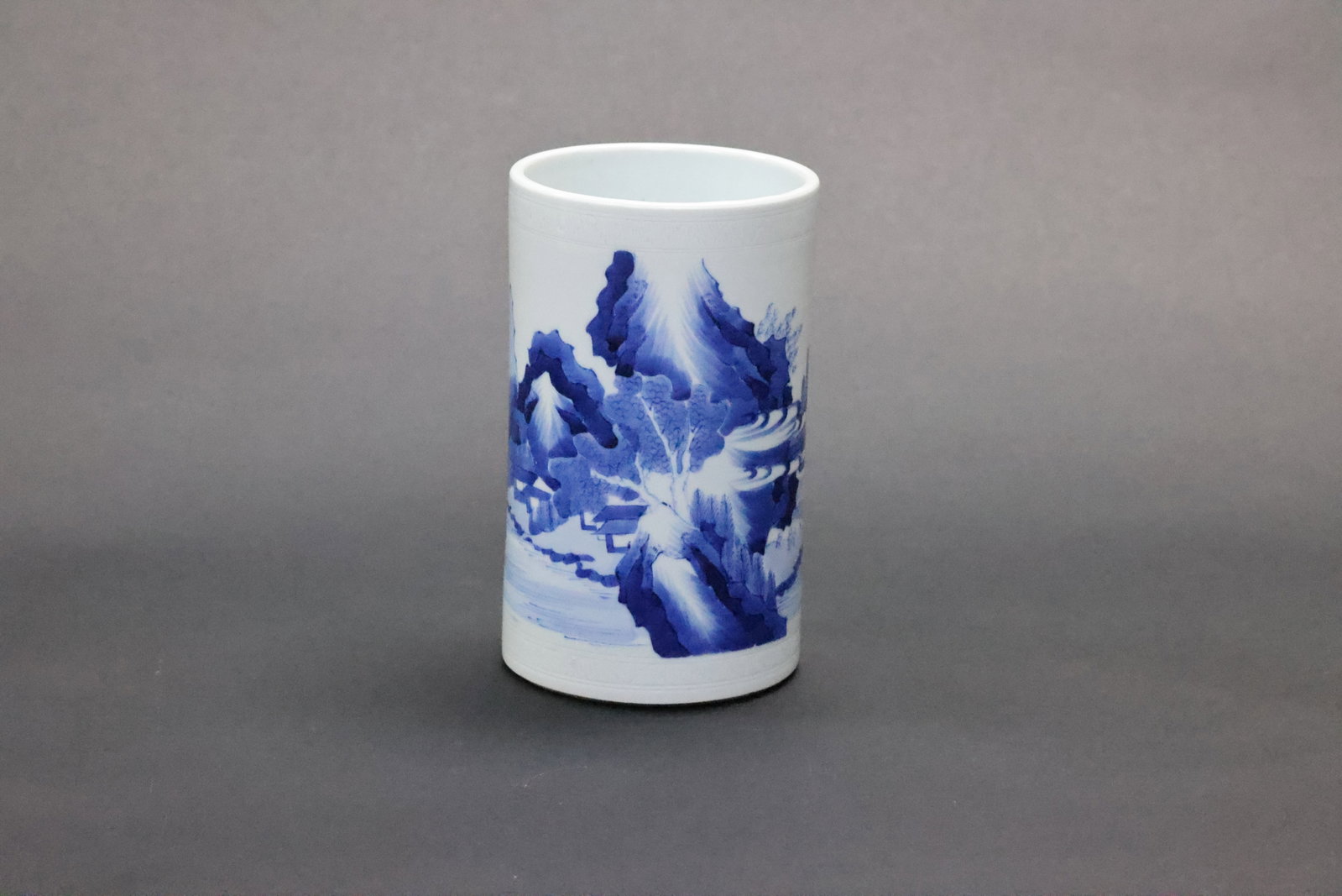 An Important 'Landscape' Blue and White Anhua-Decorated Brush Pot, Kangxi Period: Estimated Date: Mid-Kangxi period, Qing Dynasty. A blue-and-white porcelain brush pot (bitong) for the scholar's studio, produced at a private kiln.Attribution: This cylindrical blue-and-white
