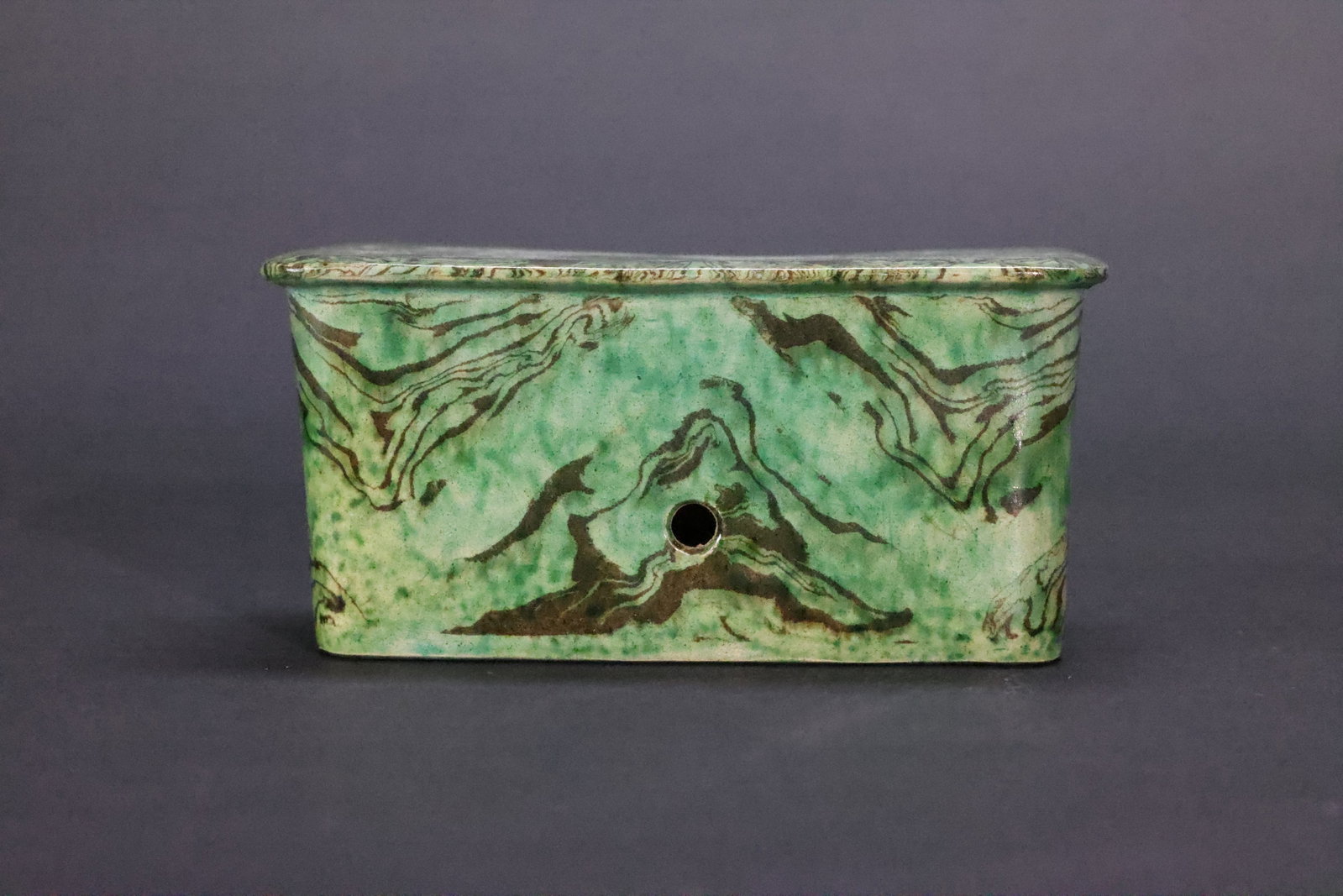 A Green-Glazed Marbled Clay Rectangular Pillow, Qing Dynasty: Estimated Date: Mid to Late Qing Dynasty. A porcelain pulse pillow (maizhen) in the archaistic marbled (jiaotai) style, inspired by Tang dynasty prototypes.Attribution: This finely modeled porcelain p