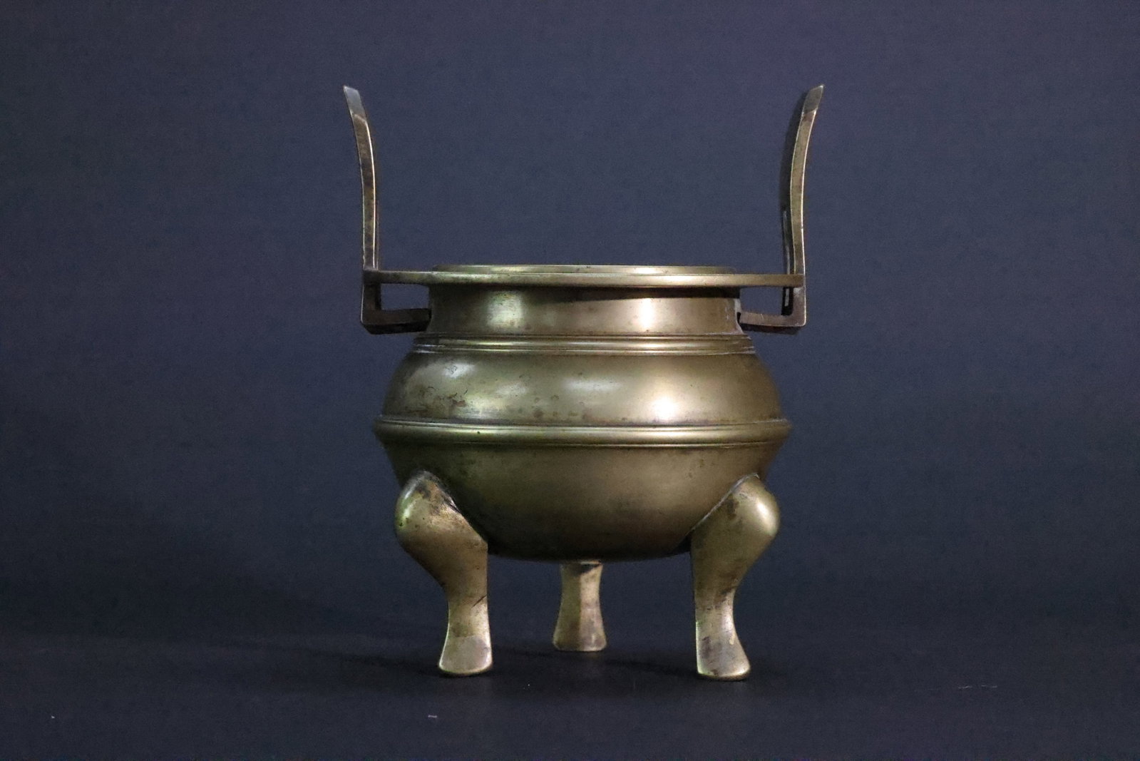 An Archaistic Brass 'Chongtianer' Bow-String Tripod Censer, Late Qing Dynasty: Estimated Date: Late Qing Dynasty. A popular brass tripod incense burner (xianglu) made for domestic devotional use.Attribution: This incense burner was cast in refined yellow brass during the late Qi