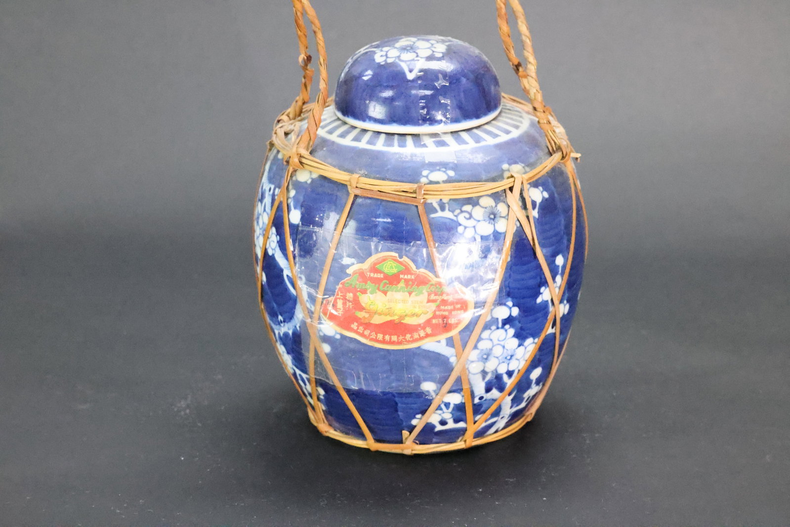 A Blue and White 'Ice-Plum' Ginger Jar with Original Wicker Handle, Early People's Republic of China: Estimated Date: 1950s–1970s. A Shanghai export blue-and-white porcelain storage jar with its original wicker carrying basket and cork stopper.Attribution: This export porcelain storage jar was produ