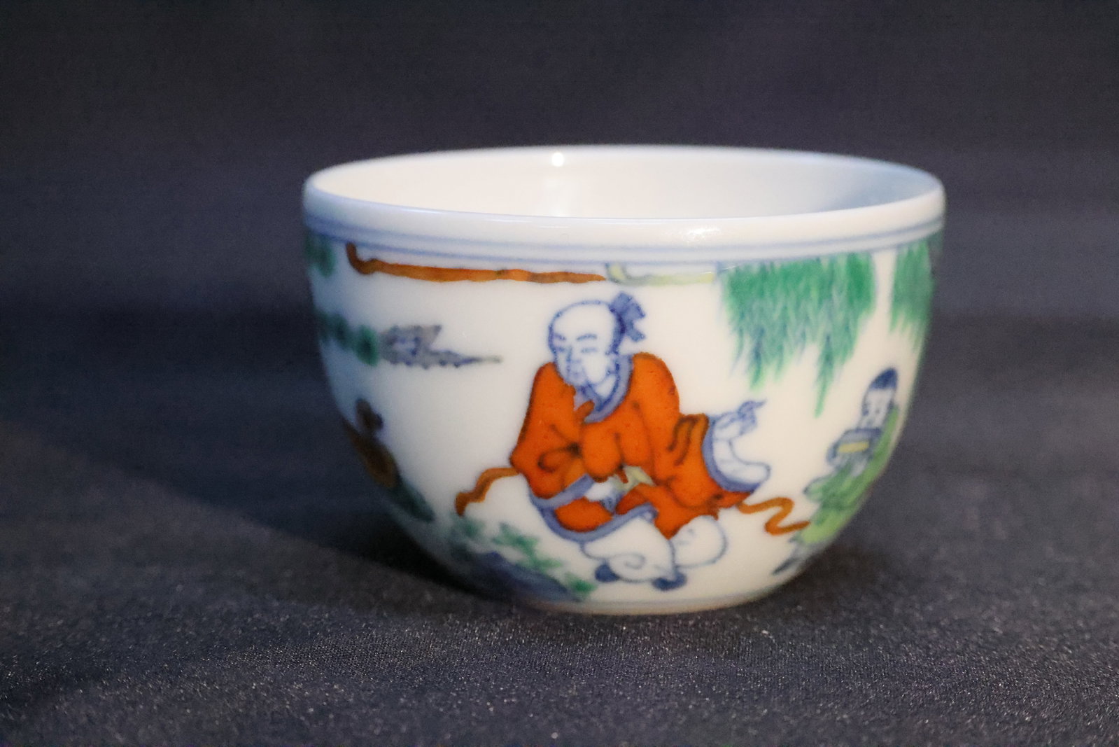 A Doucai 'Landscape and Figures' Cup: Estimated Date: Modern, bearing a Chenghua-style reign mark. A doucai 'Scholar in a Landscape' stemless cup.Attribution: This small doucai porcelain cup is finely potted in white porcelain and decorat