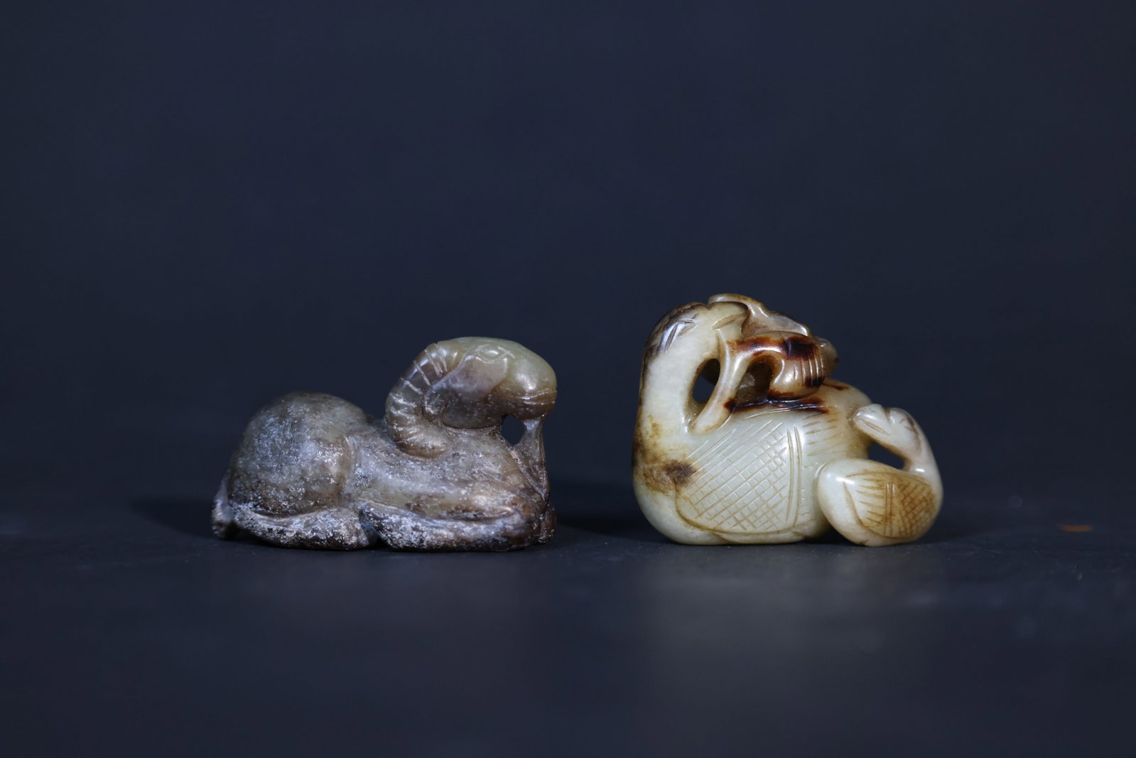 Group of Hetian (Hotan) Jade Handheld Carvings: The jade carving of a recumbent sheep is overall intact, with significant surface patina and weathering; the base shows old natural fissures but no recent chips or losses. The Hetian jade carving of