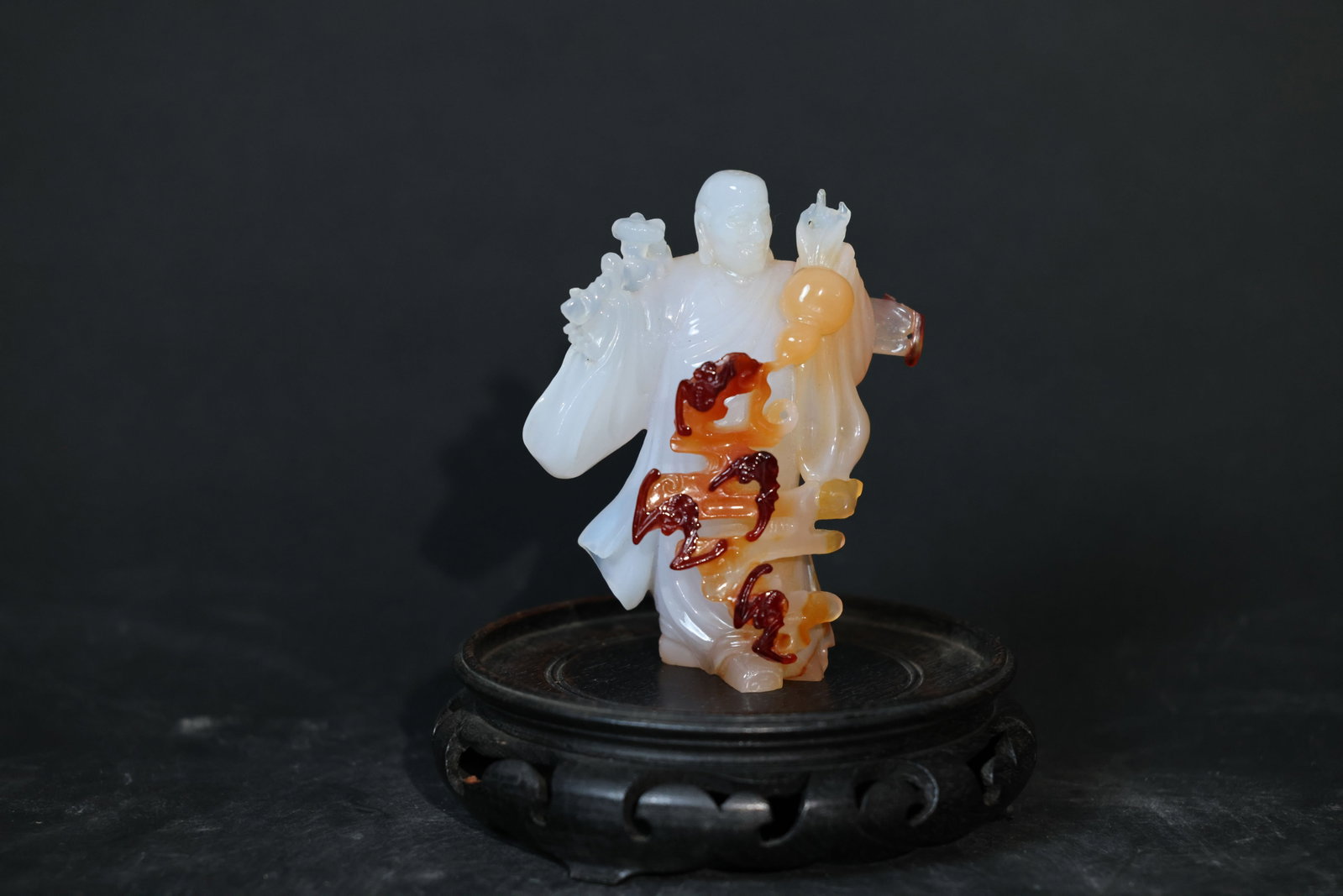 Polychrome Agate Carving: Group of Five Luohans Holding the "Shou" (Longevity) Character: Minor nicks to the surface; the agate body is free of cracks with a smooth, well-developed patina. The wooden stand shows signs of age and use. H 10.5cm W 8.5cm