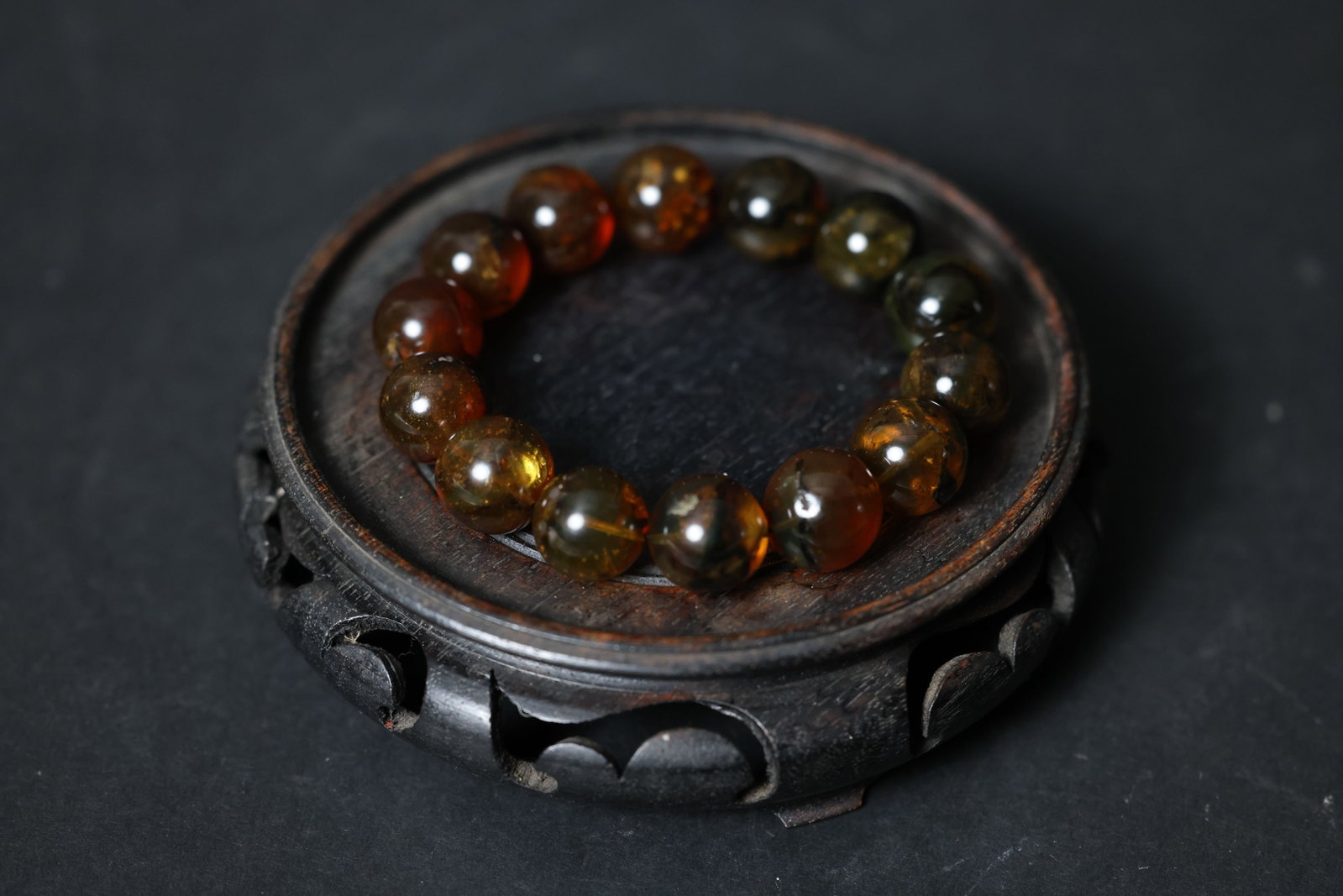 Fushun amber round-bead bracelet: Beads are intact with no chips or breaks. Several beads display natural internal fissures and ice-like cracks, with some containing visible plant inclusions. The surface shows an aged patina from