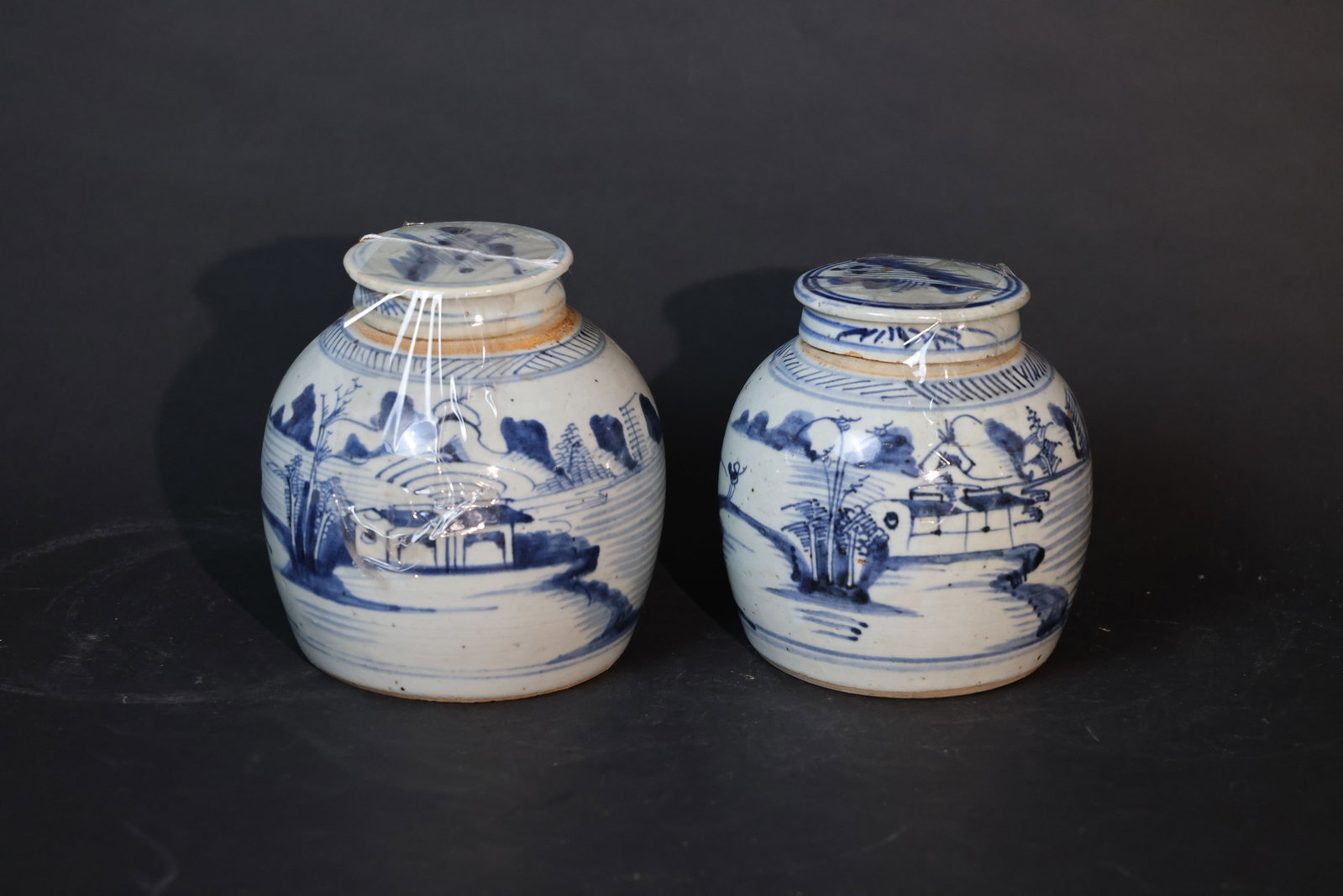 Pair of Mid-Qing Dynasty Blue-and-White Landscape "Fishermen at Leisure" Covered Jars: One jar base bears a chicken-claw mark; both lids are original and well-matched. The jars are free from through cracks, with only minor rim nicks and traces of burial earth consistent with age. H 18cm