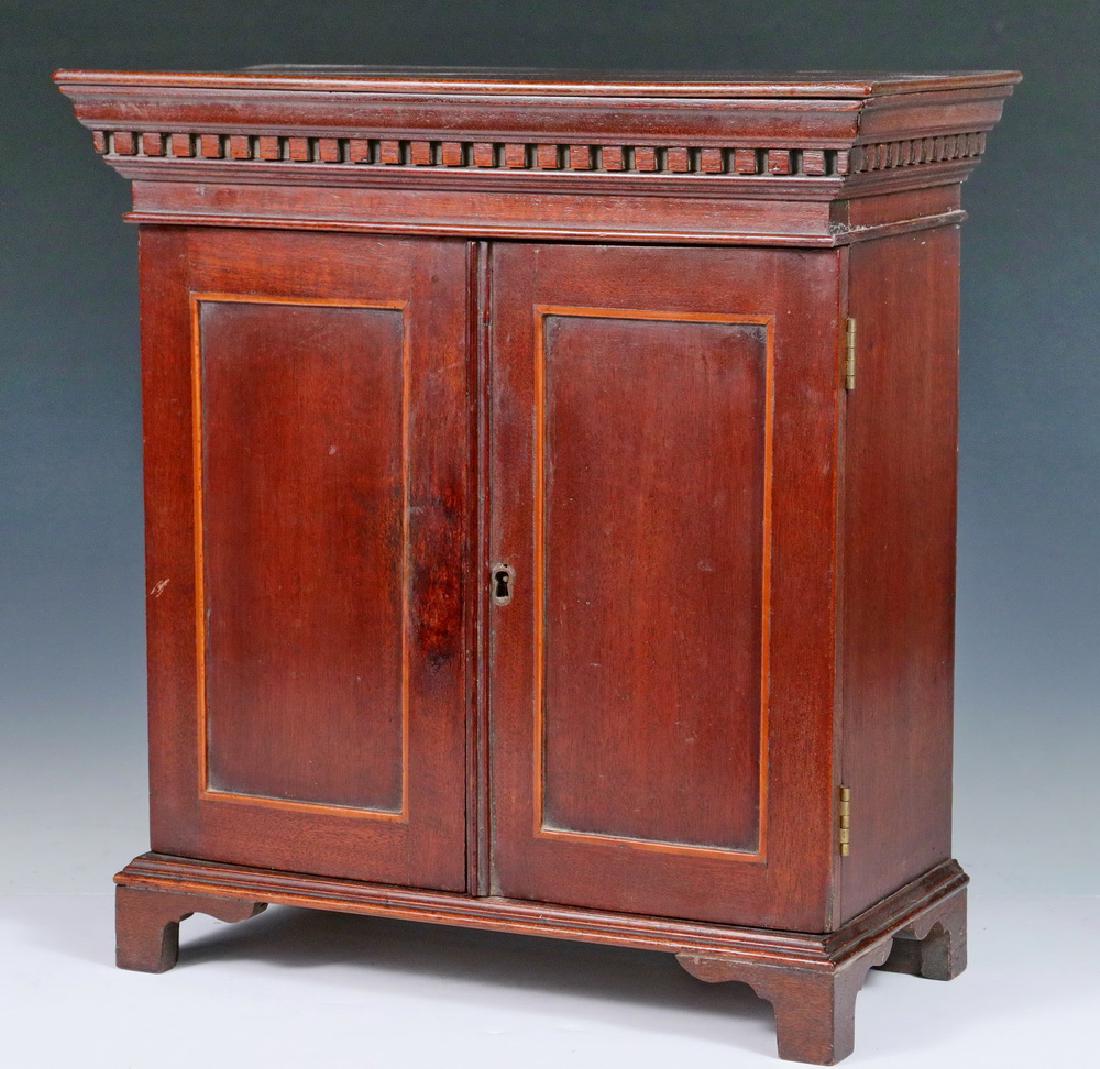 MINIATURE CABINET: Miniature Mahogany Two-door Cabinet with inset and cross banded door panels, dentil molding around top, two inside shelves, door lock (no key), 14" high, 13 1/4" x 6 1/2". Surface scratch to left door