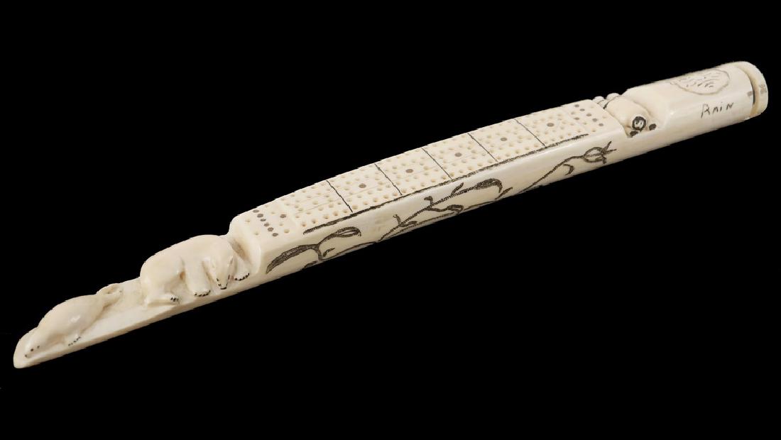 INUIT CRIBBAGE BOARD: Scrimshawn Walrus Tusk Game Board featuring a reversible "Rain/Shine" engraved man's face, vines on sides, carved figures of a man lying down in a trench at one end to hide from the polar bear and wal