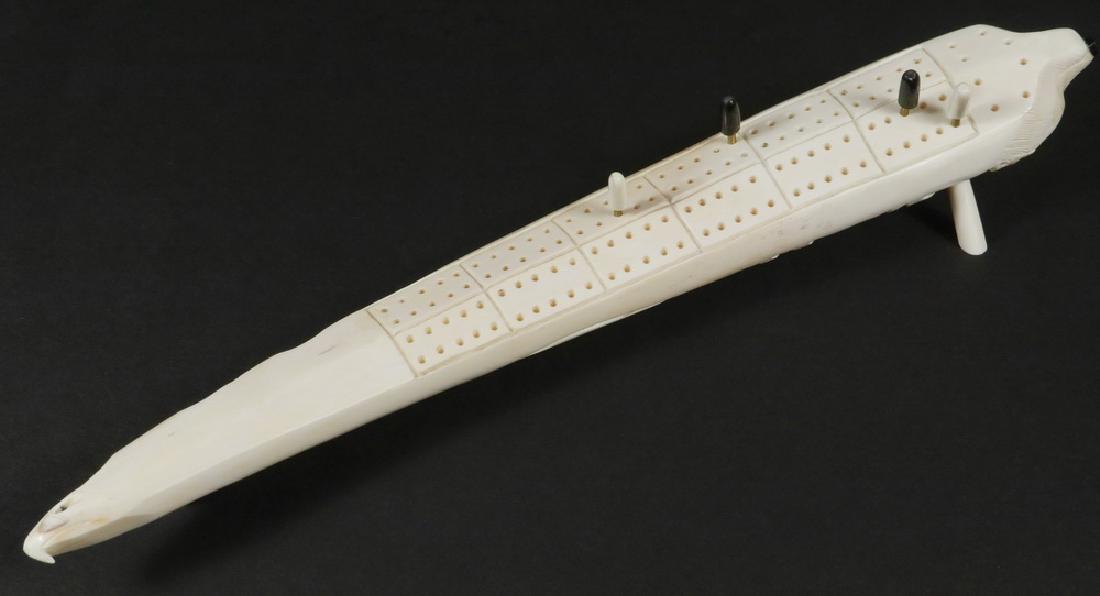 INUIT CRIBBAGE BOARD: Carved Walrus Tusk Game Board having a bear head at one end, eagle head at the other, deep relief carved wolf, seal and whale, on three feet, with four game pegs, circa 1920-1939. 17" long. Good condi