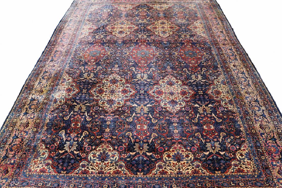 KERMAN CARPET - 12'-8" X 17 1/2': Southeast Persia, early 20th c., horizontal rows of large rosette medallions in ivory, wine red, gold, midnight blue, brick red and Persian blue on a midnight blue field, wine red vine and palmette bo