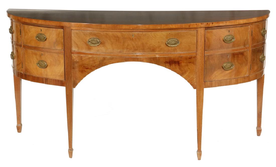 HEPPLEWHITE STYLE DEMILUNE BUFFET: Early 20th c. Hepplewhite Style Bow Front Server in figured mahogany, with banded edge overhanging top, silk-lined center drawer with lock and key, having oval brass cast bail pulls, arched apron, fla