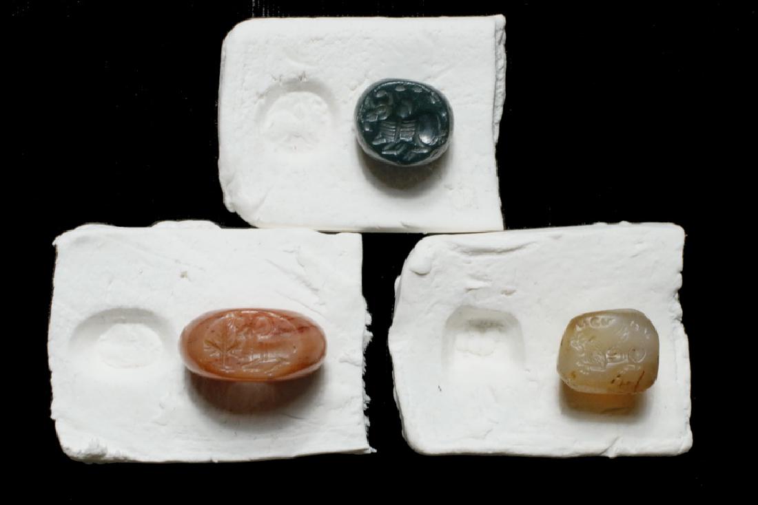 (3) ANCIENT MIDDLE EASTERN STAMP SEAL BEADS: Figural Intaglio Beads, Sasanian (Ancient Persian), 3rd -6th c. AD, including: Orange Hematite round bead with large center hole, flat oval seal featuring a reclining ram and palm tree, crescent moon,