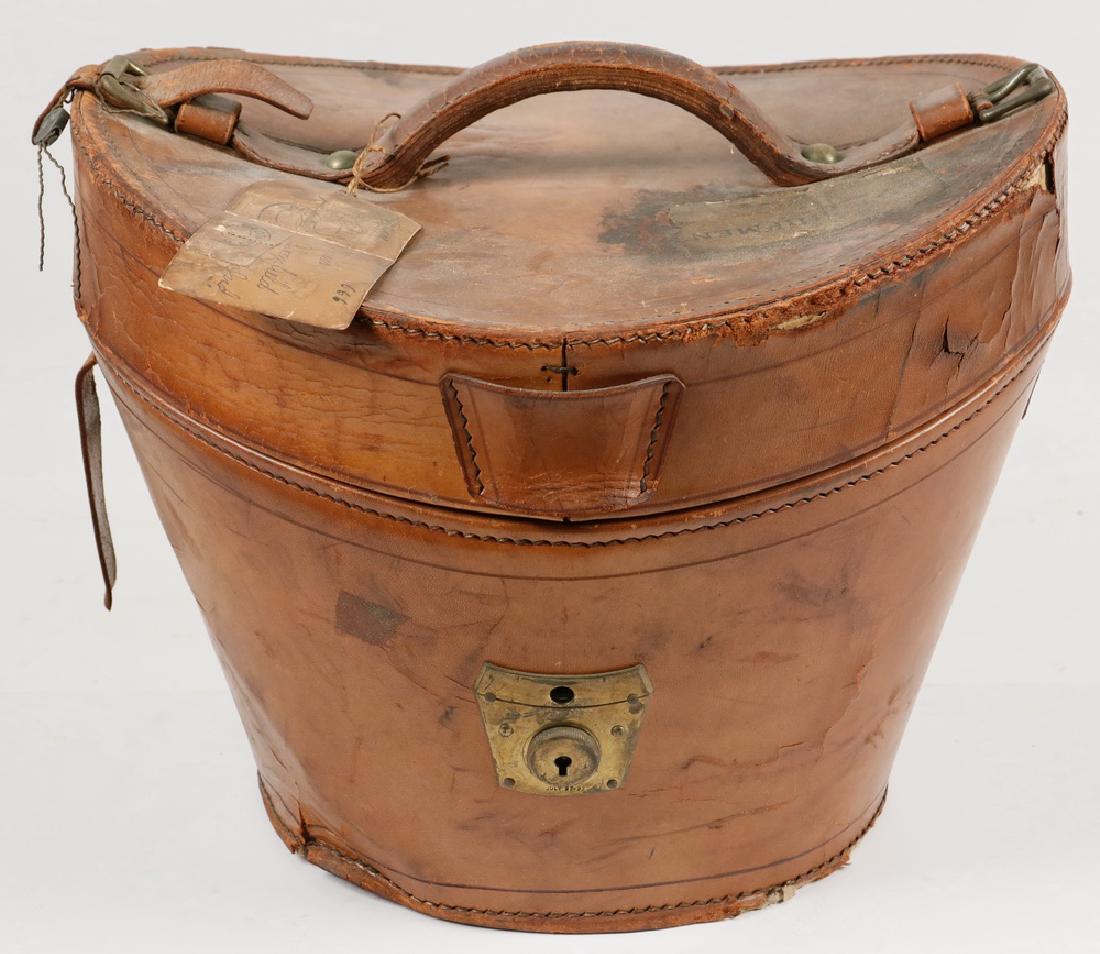 LEATHER TOP HAT CASE: Victorian Era Brown Leather Top Hat Travel Case, with red satin interior and interior leather straps, exterior with lid handle and brass escutcheon plate, inside is a black top hat from Macullar Parke