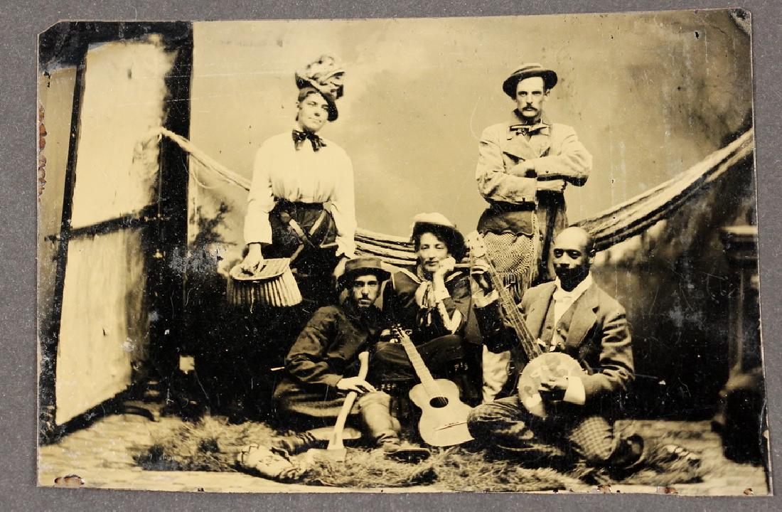 A RARE MAINE TINTYPE PHOTOGRAPH OF BLACK MUSICIAN: Tintype of Five Friends in a Rustic Studio Setting, taken circa 1885, including a Black Banjo Player (in checkered pants!), a Woman with a Guitar, a Man with an Axe, a Woman with a Fishing Creel (and 