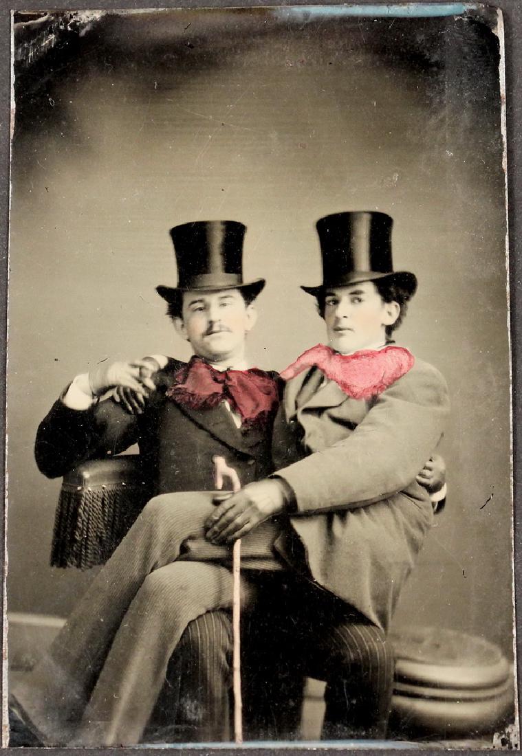 A RARE MAINE TINTYPE PHOTOGRAPH OF MEN: A Pair of Intimate Dandies, one seated in the lap of the other in spite of a second empty stool alongside, their arms around each other, clasping hands on one shoulder, the uppermost leaning back into