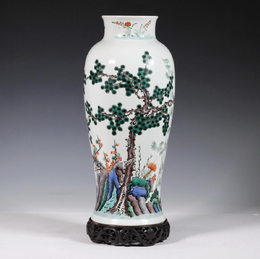 CHINESE BALUSTER VASE: Chinese Porcelain Baluster Vase on Carved Wooden Stand, 20th c., hand painted with pine tree, floral and bamboo greenery, floral spray to neck, with an ornately carved wooden stand with openwork apron