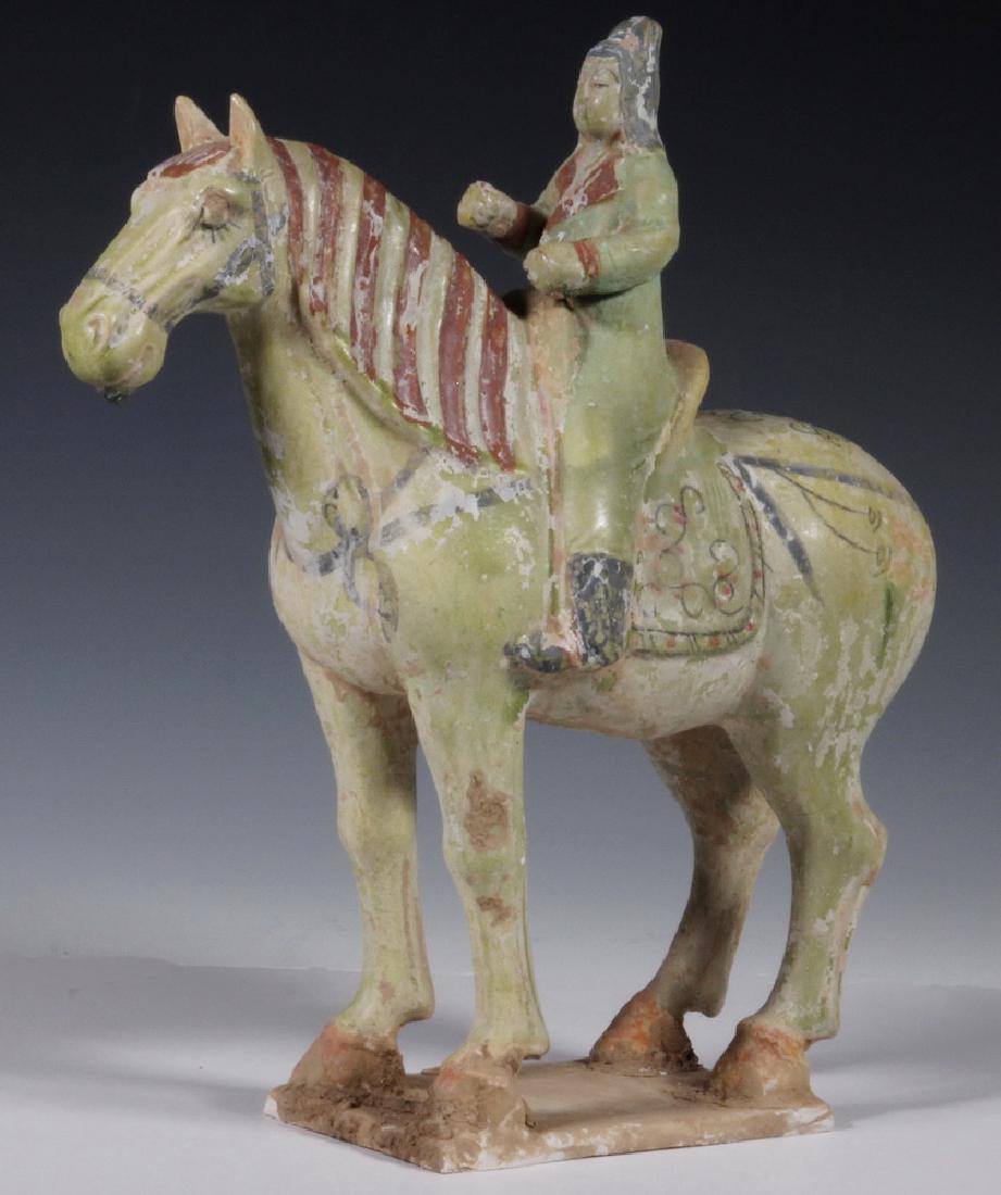 TANG POTTERY HORSE WITH FEMALE RIDER: Unfired Pottery tomb Figure, circa 700 AD, probably Xinjiang, in the far northwest of China, having polychrome decoration with celadon base, some cartooning, 11" x 11" x 4". Encrusted.