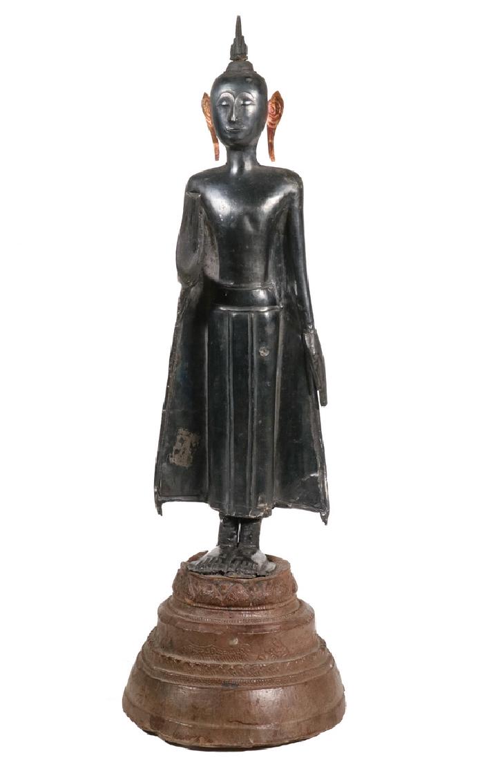 18TH C. THAI SILVER STANDING BUDDHA ON STONE BASE: Late Ayutthayah Period, silver over wood, painted hands and flame of enlightenment, with refined features, later pressed copper ears,15 1/2" tall overall. Repaired at ankles.