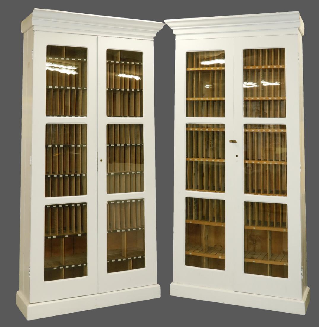 PR OF ARCHITECTURAL SORTING CABINETS: Circa 1920, in white enamel painted pine, glass doors, molded cornice and base, eight shelves with multiple vertical partitions, 88" tall 42" x 16" at base, 18" deep at cornice, 8" between shelves. Go