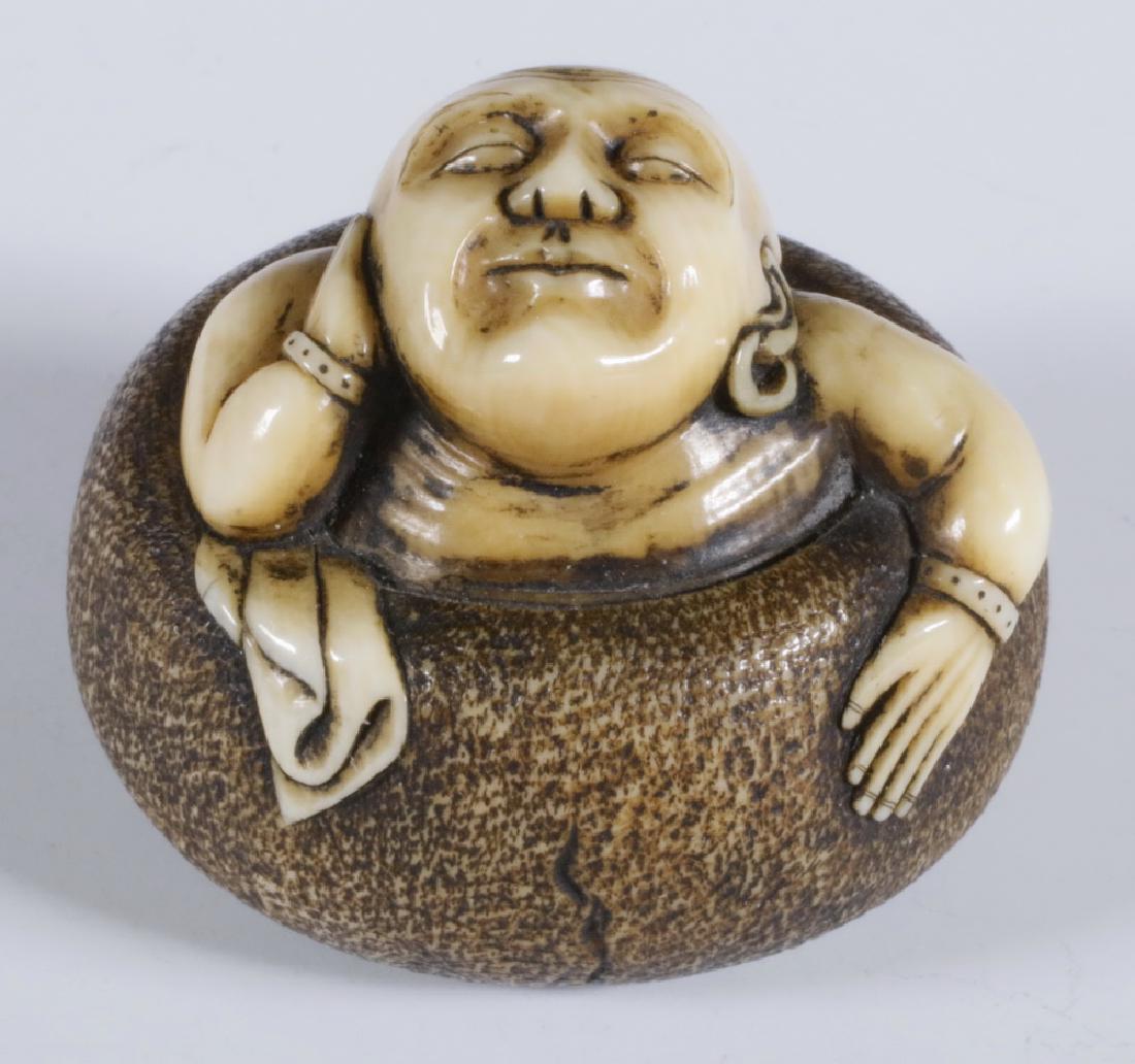 19TH C. CARVED NETSUKE OF DARUMA: Meiji period whimsical depiction of a Daruma in a hibachi form tub, wearing earring and bracelets, 1 1/4" diam. Very good condition. Provenance: From the estate of Nancy Hamilton.