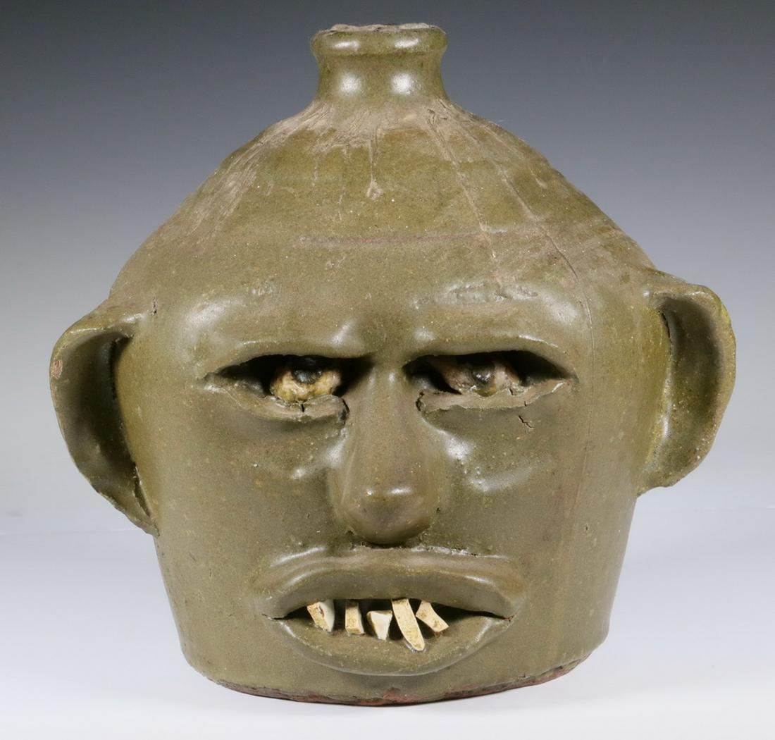 SOUTHERN ROCK TOOTH FACE JUG, LANIER MEADERS (GA,: Southern Stoneware Face Jug, wheel thrown with applied features, matte olive green glaze, deep set stone eyes and five stone teeth, base with incised script monogram 'L.M.', 8 1/4" high, 8 1/2" diam.