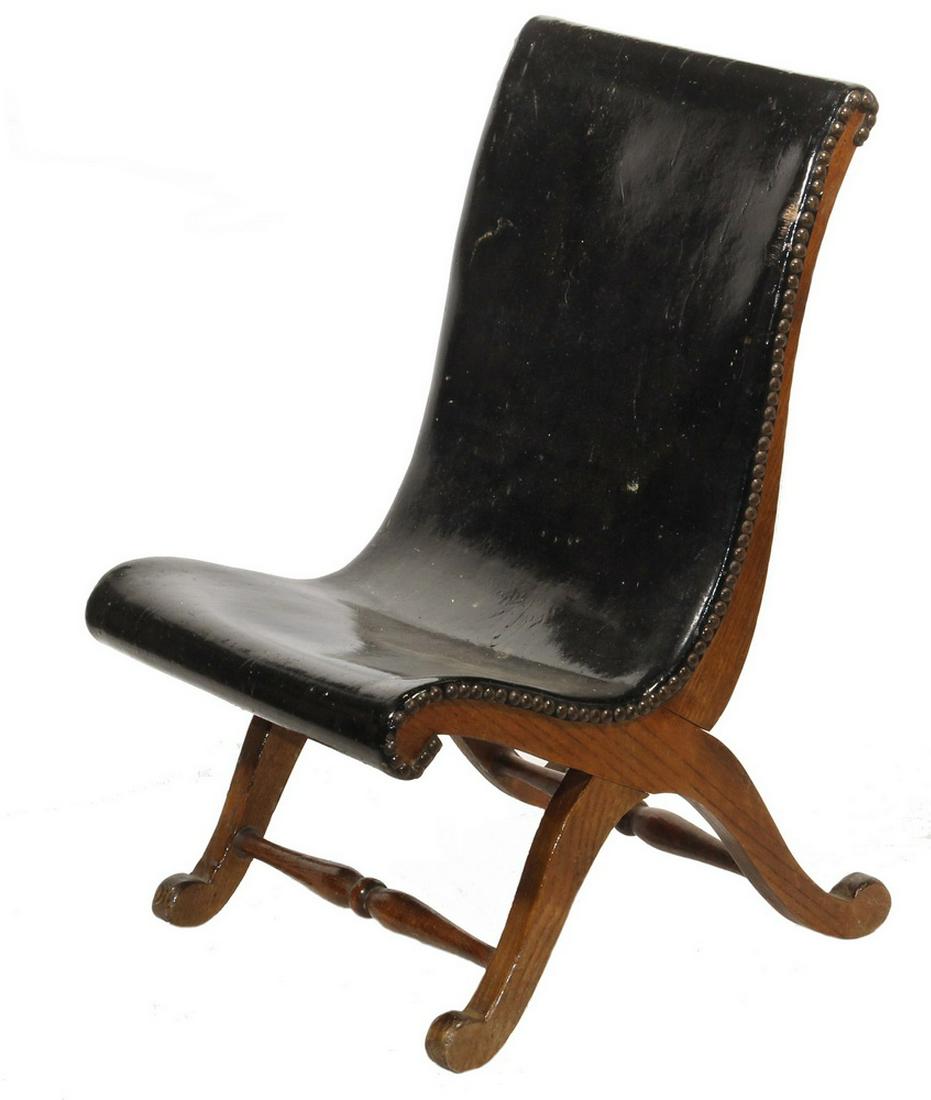 RARE CHILD'S CAMPECHE OAK CHAIR: 19th century, American, possibly Louisiana, a diminutive oak chair with rolled crest and shaped black leather brass-tacked back and seat on a curule base with turned stretchers terminating in rolled f