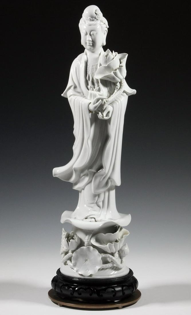 BLANC DE CHINE GUANYIN: Large Dehua Porcelain Standing Guanyin Figure, clad in flowing robes and with a contemplative expression, she is standing on a pedestal holding a lotus flower with trailing lotus blossoms below, affix