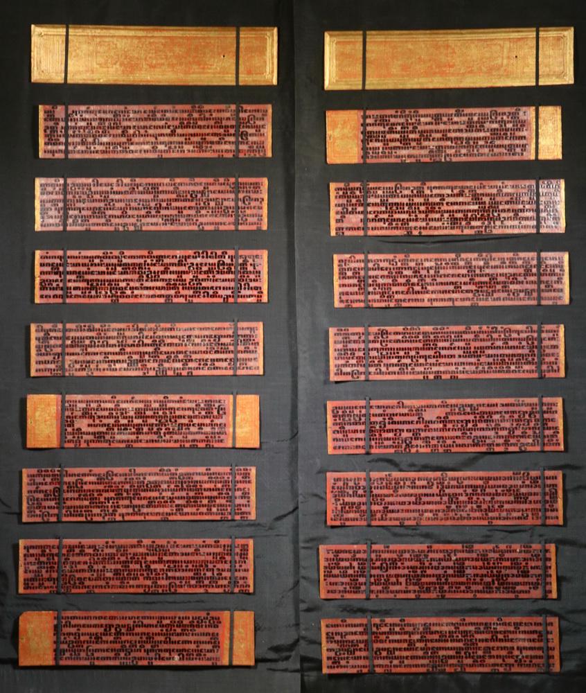 TIBETAN PRAYER BOOK WITH DISPLAY HANGERS: (2) Custom Banners holding A Tibetan Prayer Book consisting of sixteen leaves and two covers, in gold, silver, black and red lacquer, having raised text, each leaf being 4 1/2" x 19 1/2", banners are