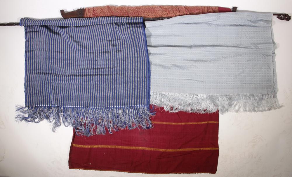 (4) INDONESIAN TEXTILE WALL HANGINGS W/ WOODEN HANGERS: Collection of (4) Indonesian Fabric Wall Hangings, with carved wooden hangers, including: Red & blue silk, with fringed ends, 32 1/4" wide, 82" long (w/o fringe), 35 3/4" wide, 7 1/2" long wooden hang