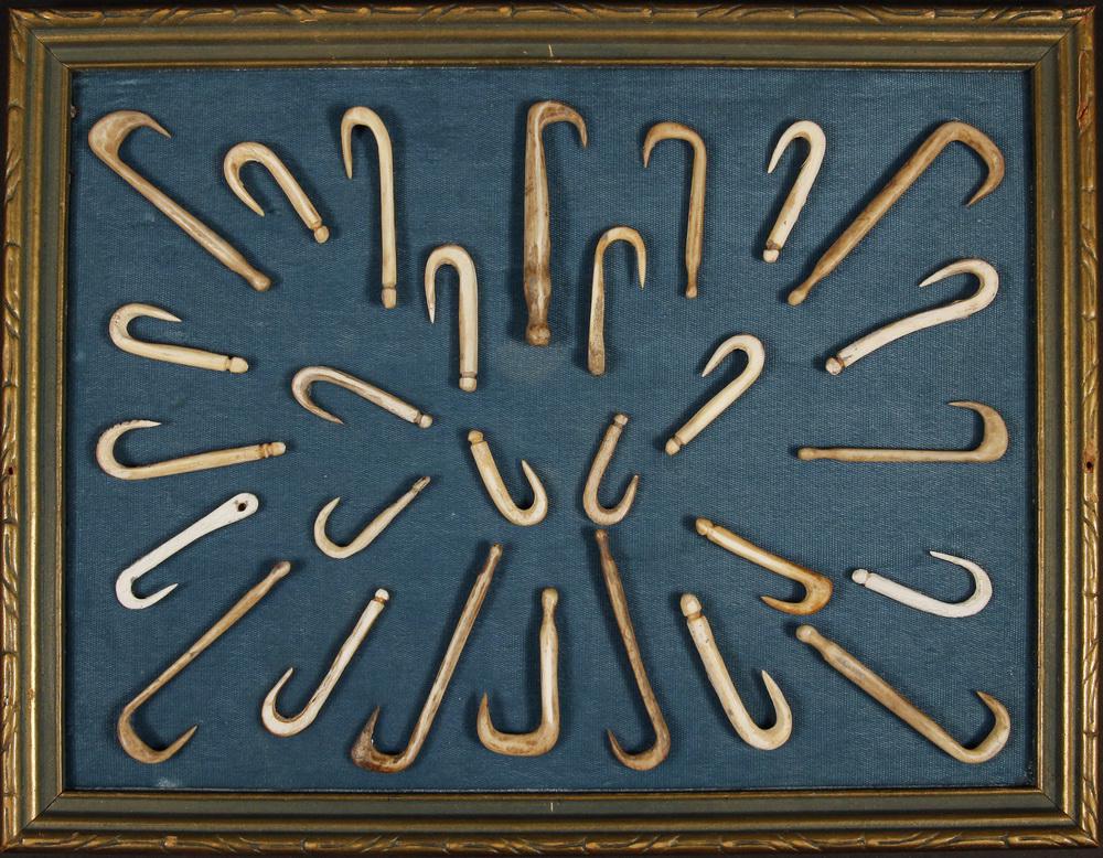 FRAMED COLLECTION OF INUIT FISHING HOOKS: (27) Carved Bone Fishing Hooks, late 19th - early 20th c., mounted on green cloth in a green and gold molded stick frame, ranging from 1 1/4" to 3" long, 10" x 13" frame. Good condition. Provenance: F