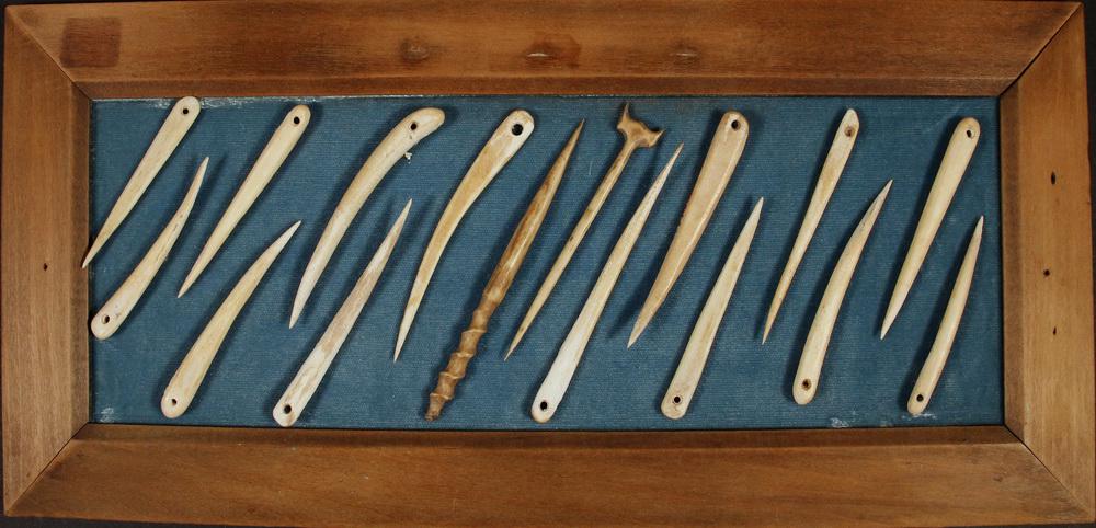 FRAMED COLLECTION OF INUIT SEWING NEEDLES: (16) Carved Bone Sewing Needles, mounted on green cloth in a stained pine mitered frame. The needles are 3" to 3 1/2" long, in 7 1/2" x 16 1/2" frame. Provenance: From the estate of Paul Brouillard, C