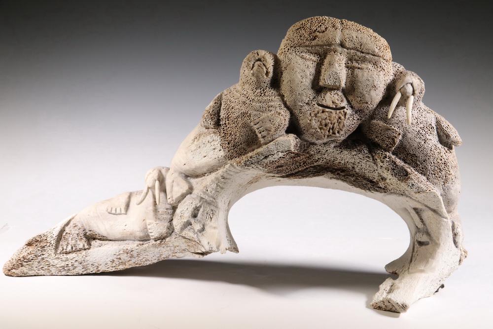 INUIT WHALEBONE CARVING BY KALLUQ PALITUQ: 'Animals' by Kalluq Palituq, Clyde River, Nunavut, Canada (born 1944), created in 2000 from ancient whalebone vertebrae, depicting walruses flanking a human face, with inserted bone tusks, 13 3/8" tal