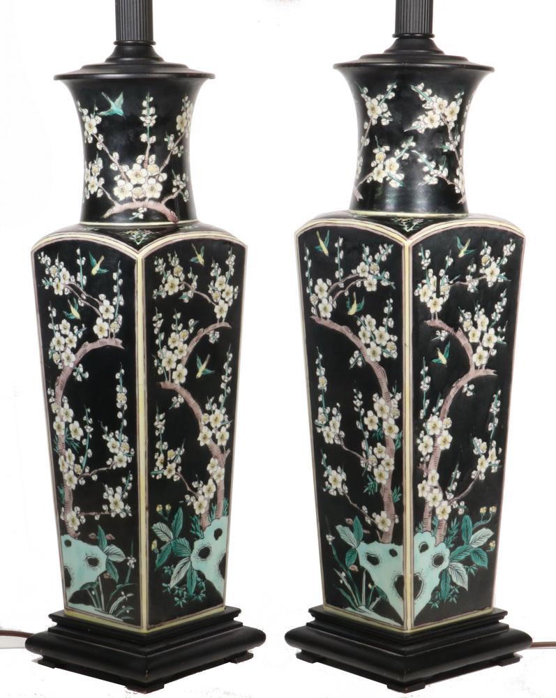 PR OF LARGE FAMILLE NOIR VASES, MOUNTED AS LAMPS: Circa 1930s Chinese Porcelain Vases, tapered square with round flared necks, decorated with polychrome flowering trees and birds over black, converted to electric lamps, with harps, on wooden bases. 2