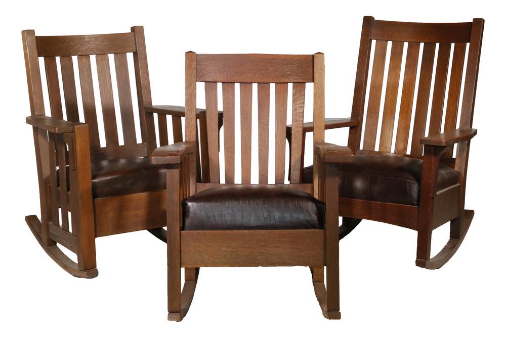 (3) ARTS & CRAFTS ROCKING CHAIRS: Craftsman Oak Rockers with fumed finishes, of various design, two L&JG Stickley and one Harden, all with brown leather drop-in sprung seats, all with arm pass-throughs, three slat arms, five or six sl