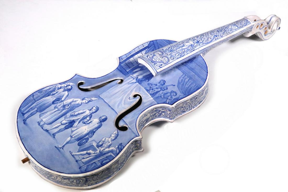 FRENCH FAIENCE VIOLIN: 19th c. French Tin Glazed Blue and White Pottery Decorative Violin, with painted scenic and figural decoration to front and back, sides with putti and vine motifs, 22 3/4" long, 8" x 4". Missing turni