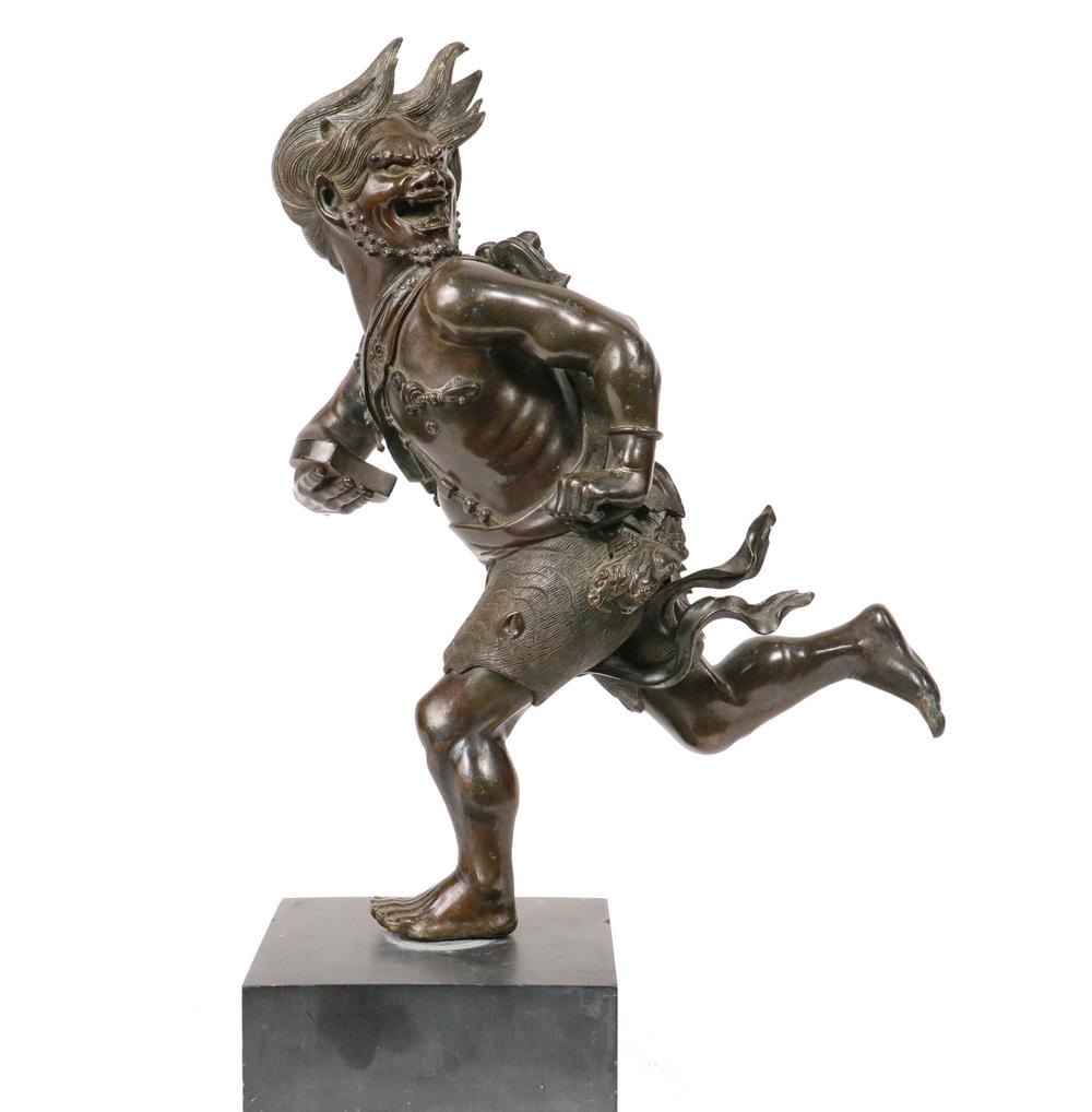 JAPANESE BRONZE SCULPTURE: Edo Period Running Demon or Oni, balanced on one foot, in full flight, his head turned over his left shoulder, a tablet in his right hand, he is wearing a dragon skin like Hercules in his lion skin, 1