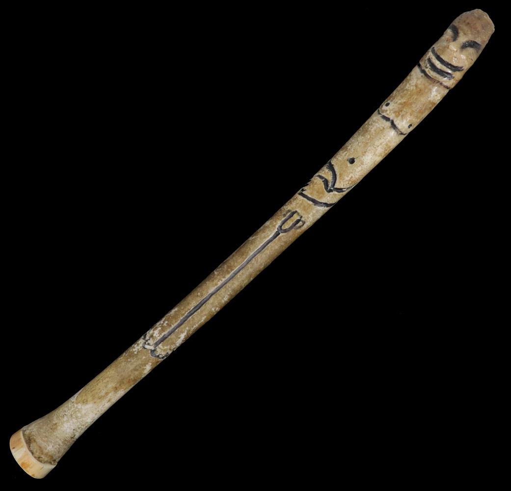 LARGE INUIT CARVED BACULUM: Seal Club made from a Walrus Baculum or penis bone, carved with the image of a smiling man having his hands crossed on his belly above his own anatomy, the incised decoration filled with black ink, a 