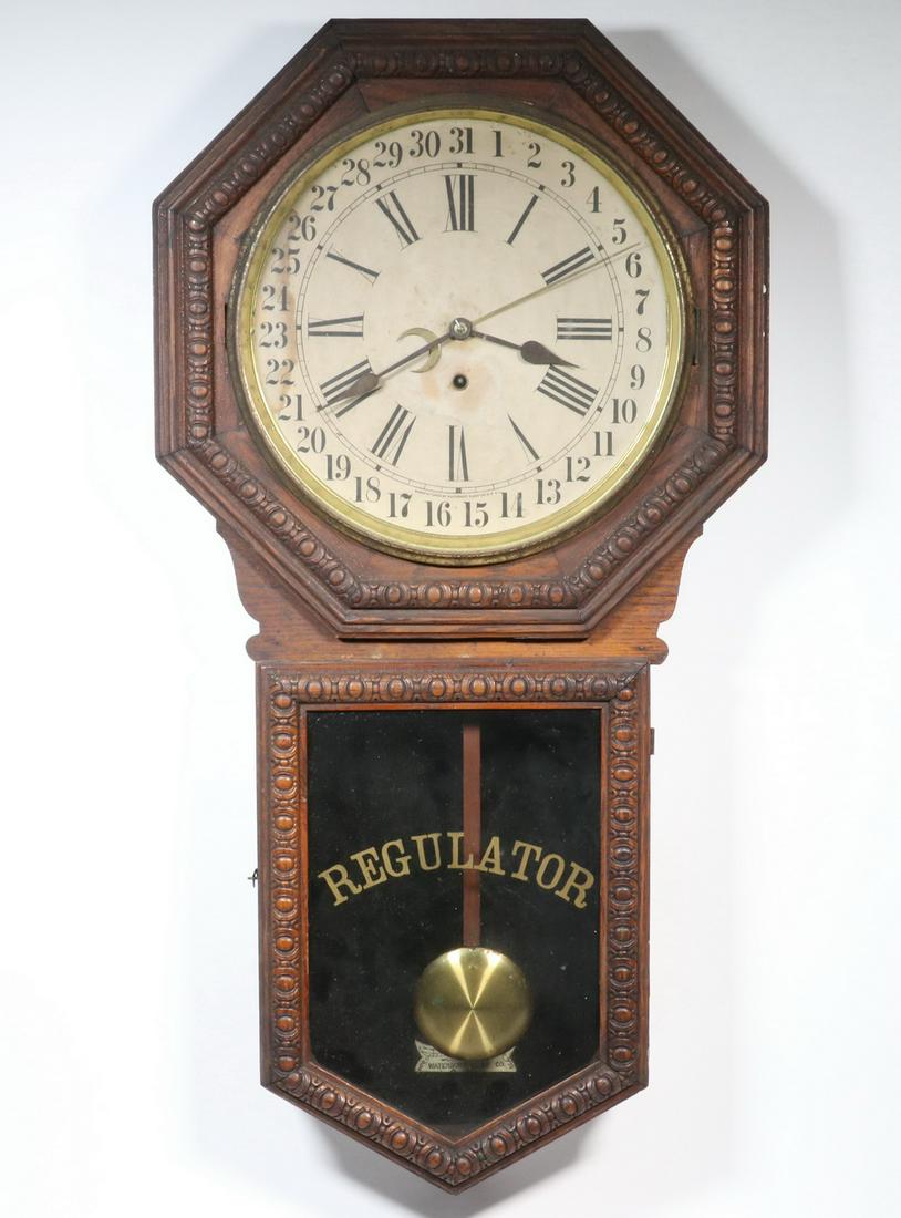 WATERBURY CLOCK COMPANY WALL MOUNTED CALENDAR REGULATOR: Oak Cased Long Drop Waterbury Regulator, 8-day time only movement with pendulum, case with embossed decorative edging, octagonal top with brass bezel, paper over metal dial marked 'Manufactured by Wat