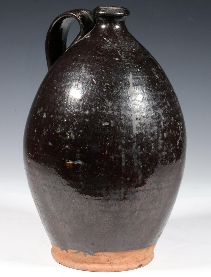 OVOID REDWARE JUG: Large Early 19th c. Redware Jug, with deep brown glossy glaze, strap handle, unglazed base edge, 12" high, 6 1/2" diam. Small side nick to handle, foot edge flakes, surface wear.