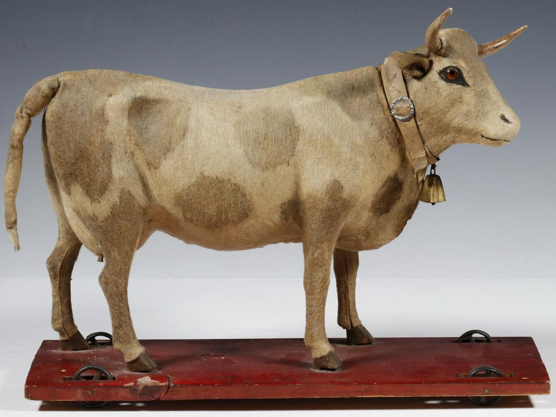 VINTAGE COW PULL TOY: German Made Composition Cow Toy, set on a wheeled wooden platform, with glass eyes and bell, designed to 'moo' when head is moved to the right (no longer functioning), 9 1/4" high, 12 1/8" x 4 1/4". H