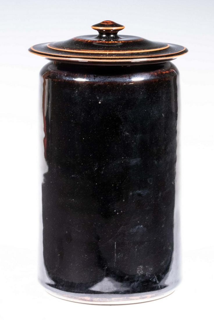 BROTHER THOMAS BEZANSON (CANADA/VT, 1929-2007) ART: Covered Jar in Tenmoku Glaze, 1970s, cylindrical shape wide overhanging lid, base incised "Benedictine Monks, Weston, Vermont" and with BT's cipher, 10" high, 5 3/4" diam. Good condition.