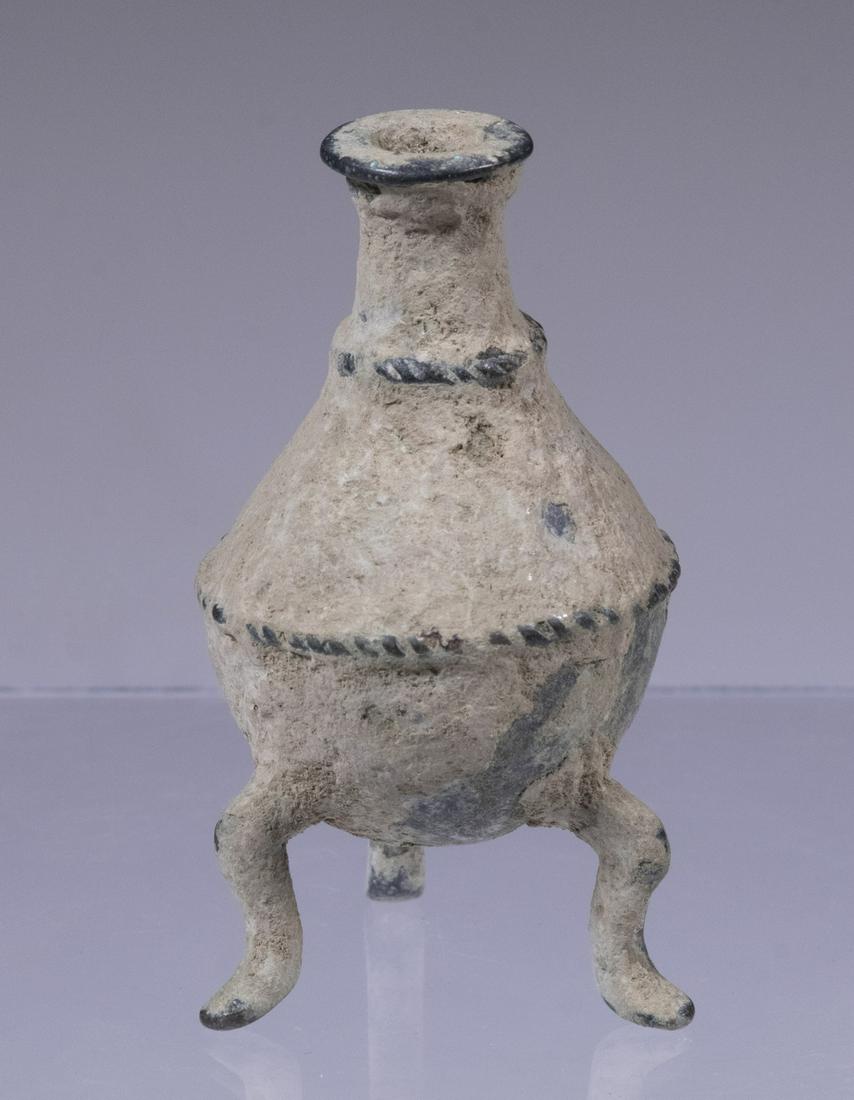 ANCIENT BRONZE ROMAN BOTTLE ON THREE LEGS: Circa 1st c. BC. Used for perfume/medicine/cosmetics, having 'roped' trim, flexed legs, 2 1/2" tall, encrusted with verdigris.