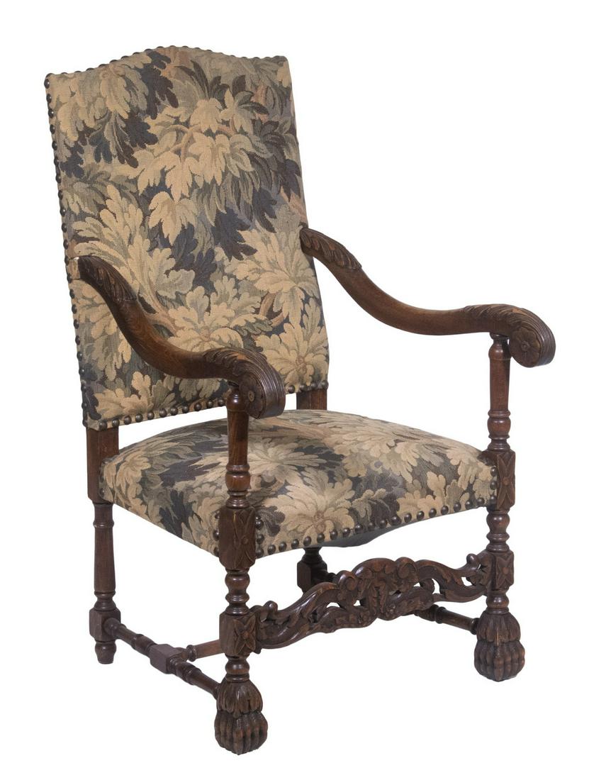 FLEMISH STYLE ARMCHAIR: 1900's vintage, upholstered in a foliate tapestry with large brass domed tacks rimming the edge of the arched back, open arms with leafy carvings, scrolled ends resting on ring turned urn stanchions, 