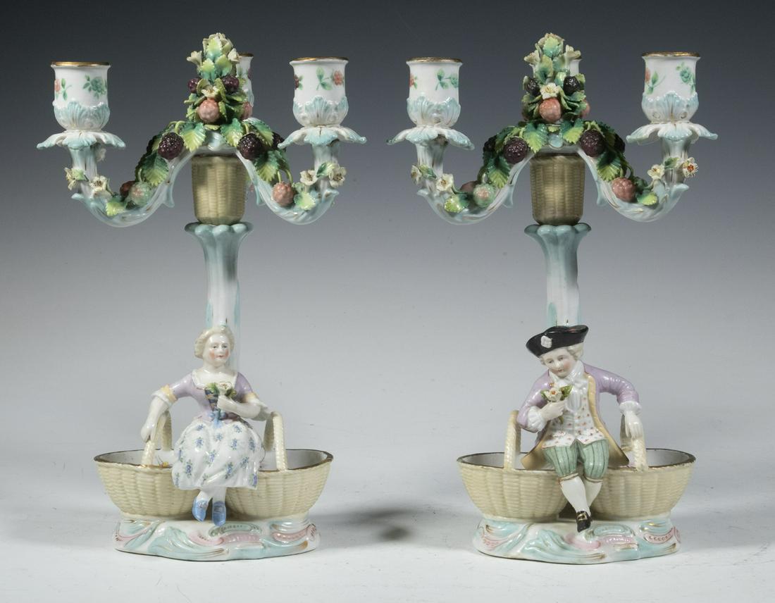 PR PORCELAIN CANDELABRA, MARK OF JOSEPH-GASPARD ROBERT: Pair of Continental Figural Three-Light Candle Holders, the tops with intricate fruit and floral decoration supported by a central basket, each oval base with a double basket and a seated figure in 18