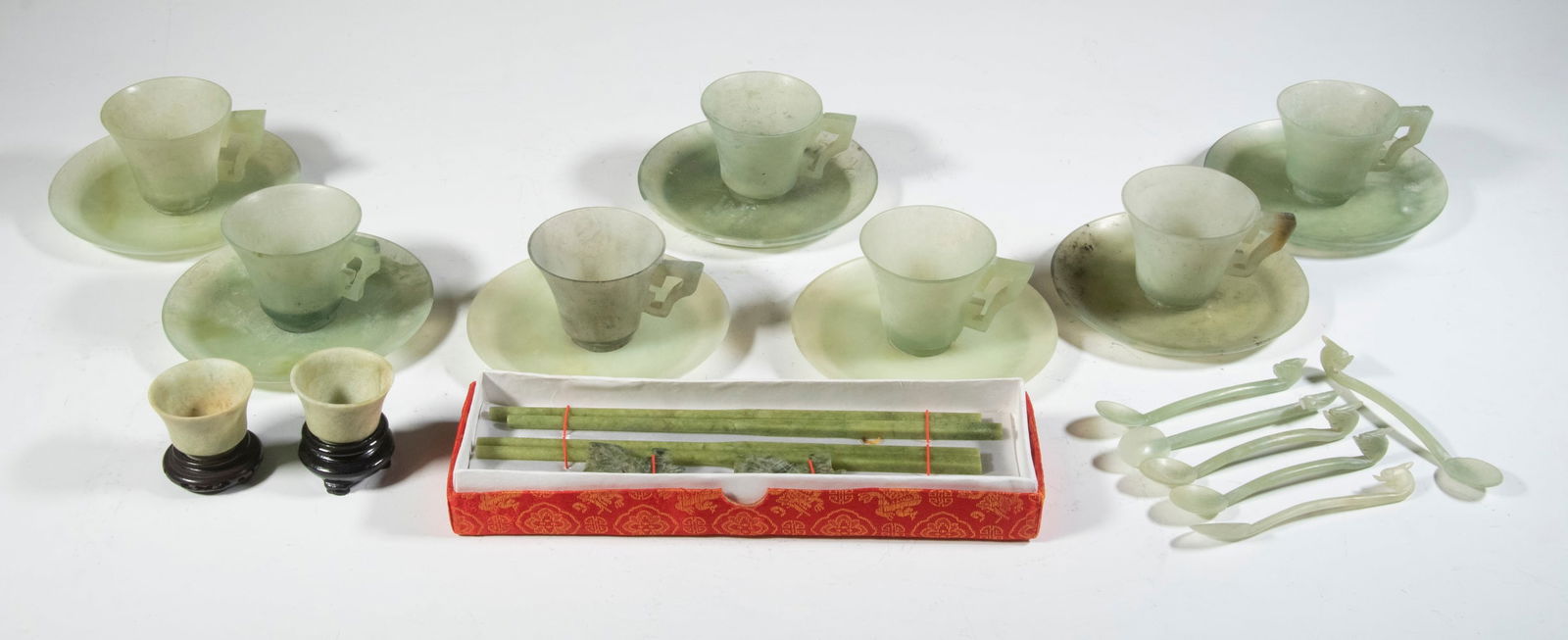 CARVED JADE CUPS, SAUCERS & ACCESSORIES: (24) Piece Lot of Chinese carved celadon jade serving items, incl: (7) Cups, 2" high; (7) Saucers, 4 3/4" diam.; (6) Spoons with dragon head handles, 4 1/4" long; (2) Wine cups, each with a wooden sta