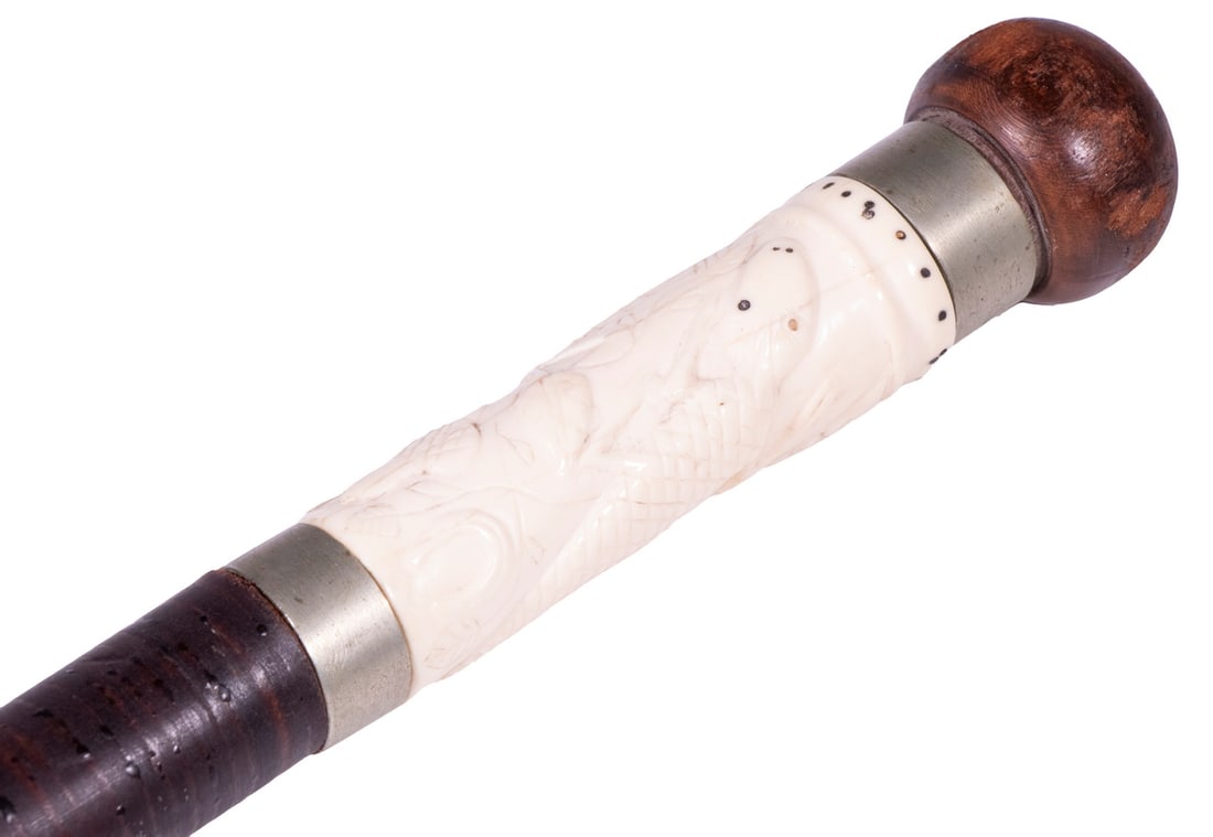 STACKED LEATHER CANE WITH ALLIGATOR CARVED PANEL: Late 19th c. Gentleman's Walking Stick, having an inset carved ivory panel depicting an alligator, branches with acorns and horseshoe, and ball form wooden top, brass tip, 35" long.