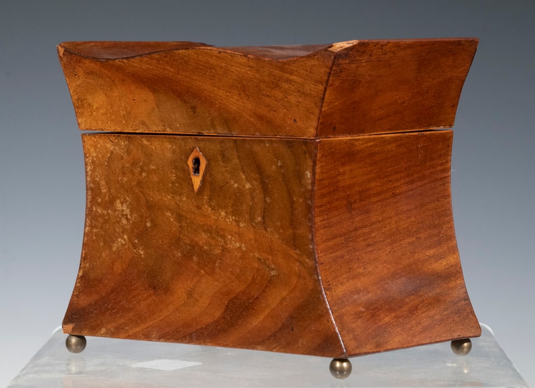 SMALL MAHOGANY TEA CADDY: 19th c. Shaped Tea Box, in figured mahogany with inlaid escutcheon and lid decoration, set on ball form metal feet, single felt lined interior compartment, 5" high, 6" x 4". Minor veneer chips.