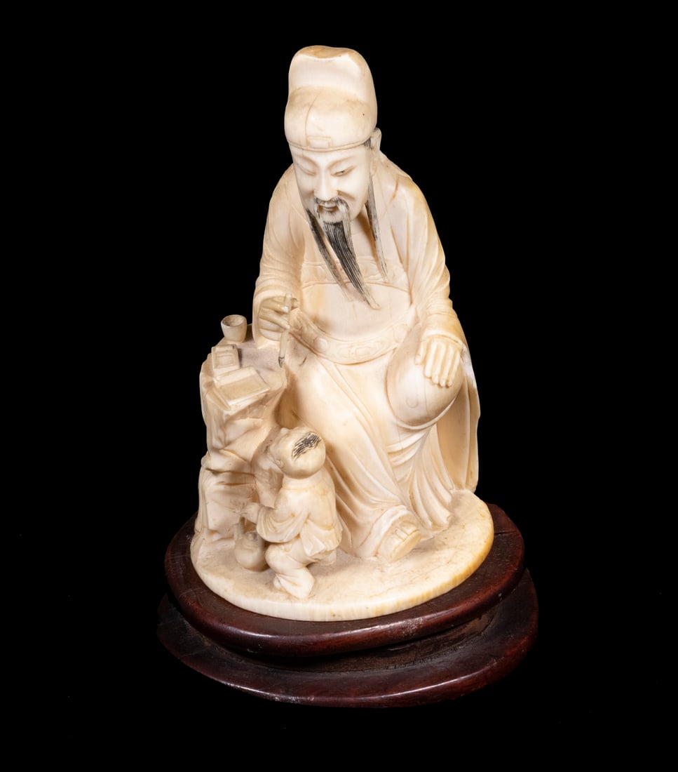 19TH C. JAPANESE OKIMONO: A Confucian Scholar seated in a scholars stone surround, brush in hand, an acolyte with tea pot at his knee, mounted on oval wooden base, 5" tall figure only, 6" x 3 1/2" x 3" overall, yellowing, soil