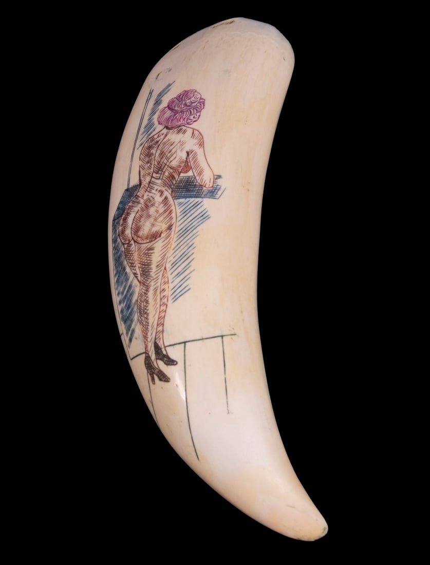 SCRIMSHAWN WHALES TOOTH: Full-length Portrait of a red-headed nude woman in black pumps, viewed from behind while leaning out an open window, with red, flesh and blue inking, 7" long.
