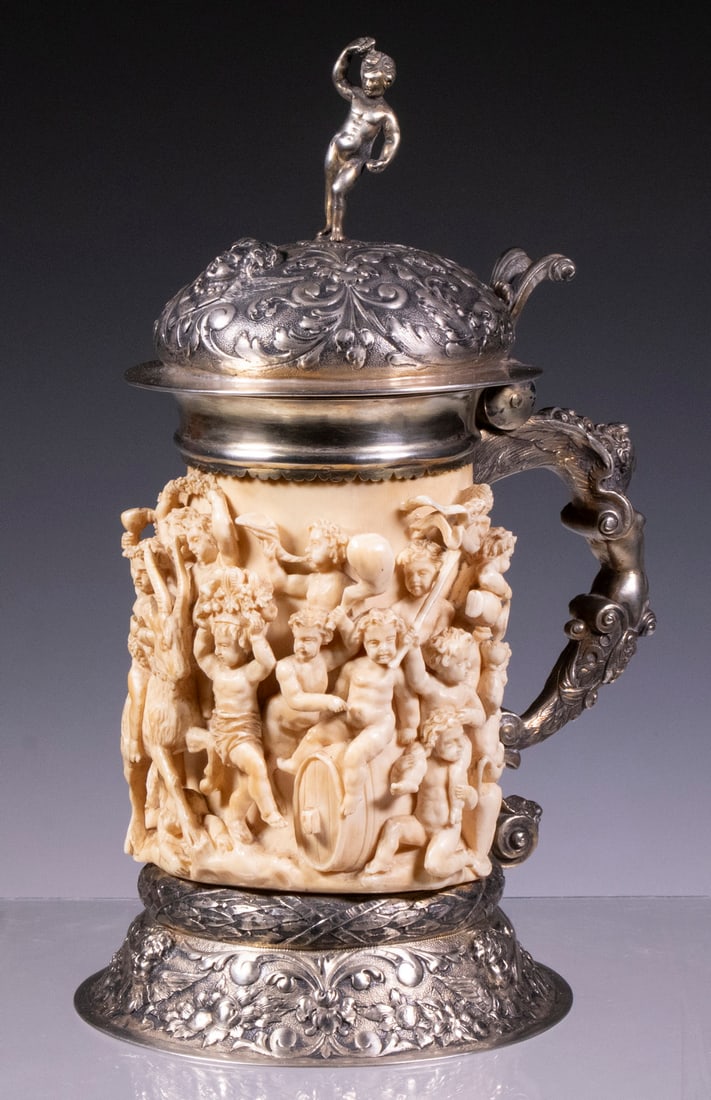 18TH C. GERMAN IVORY AND GILT SILVER LIDDED TANKARD: The ivory body carved in deep relief with the population of a Baccanale with festive putti riding a goat, a cask, and each other, festooned in floral garlands and crowns, pouring wine, waving the pine